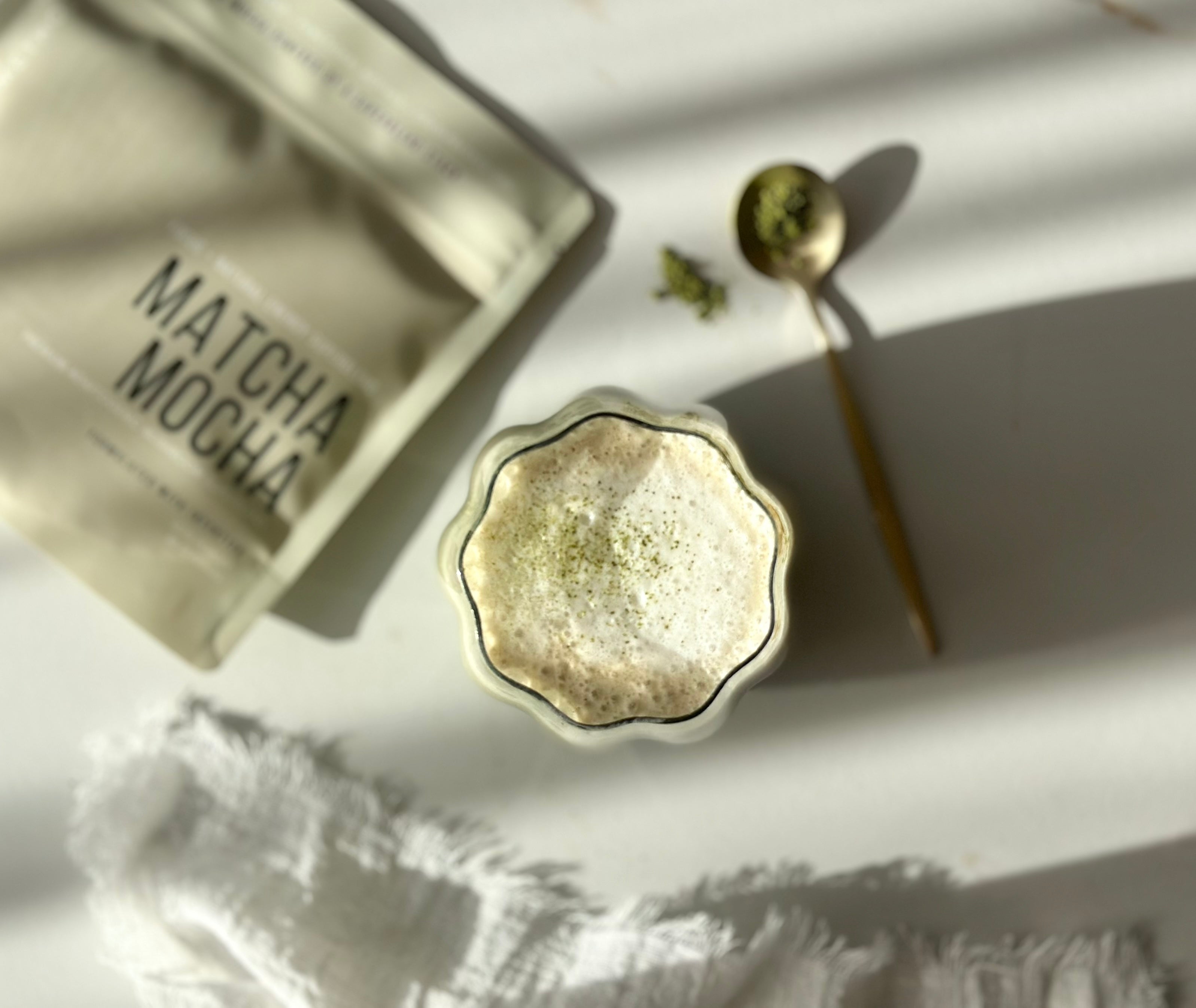 Matcha Mocha · Precision lifestyle — fluted glass matcha latte with gold spoon, soft natural light.