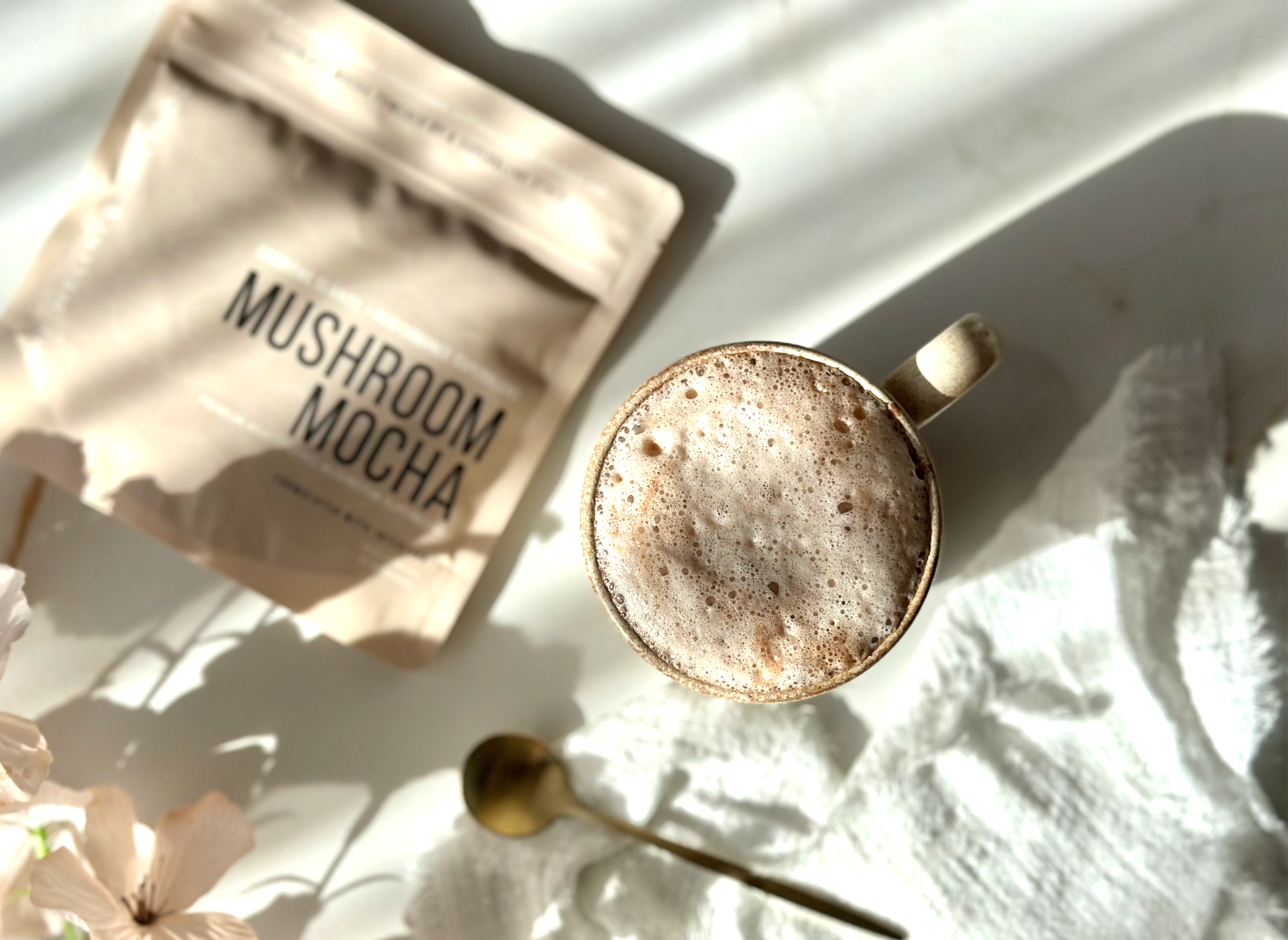 Mushroom Mocha · Foundation lifestyle — warm cacao mocha in a stoneware mug beside the pouch, soft morning light, florals.