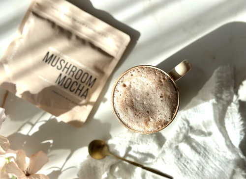 Mushroom Mocha · Foundation lifestyle — warm cacao mocha in a stoneware mug beside the pouch, soft morning light, florals.